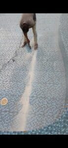 عامل يستخدم أداة كهربائية على مسار في أرضية مسبح مكسوة بالبلاط.